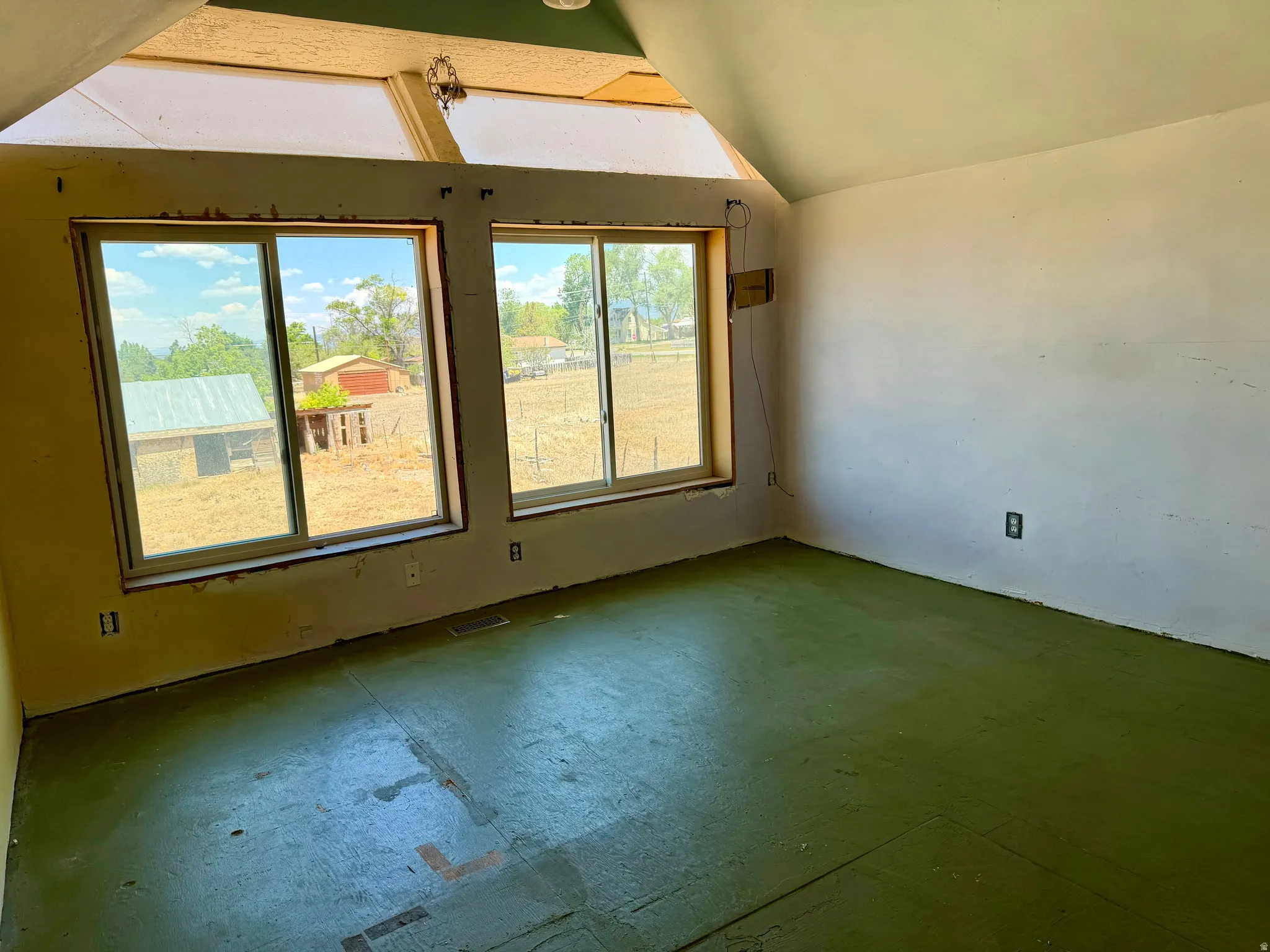 Room featuring multiple windows, a sloped ceiling with exposed structural elements, and an unfinished floor