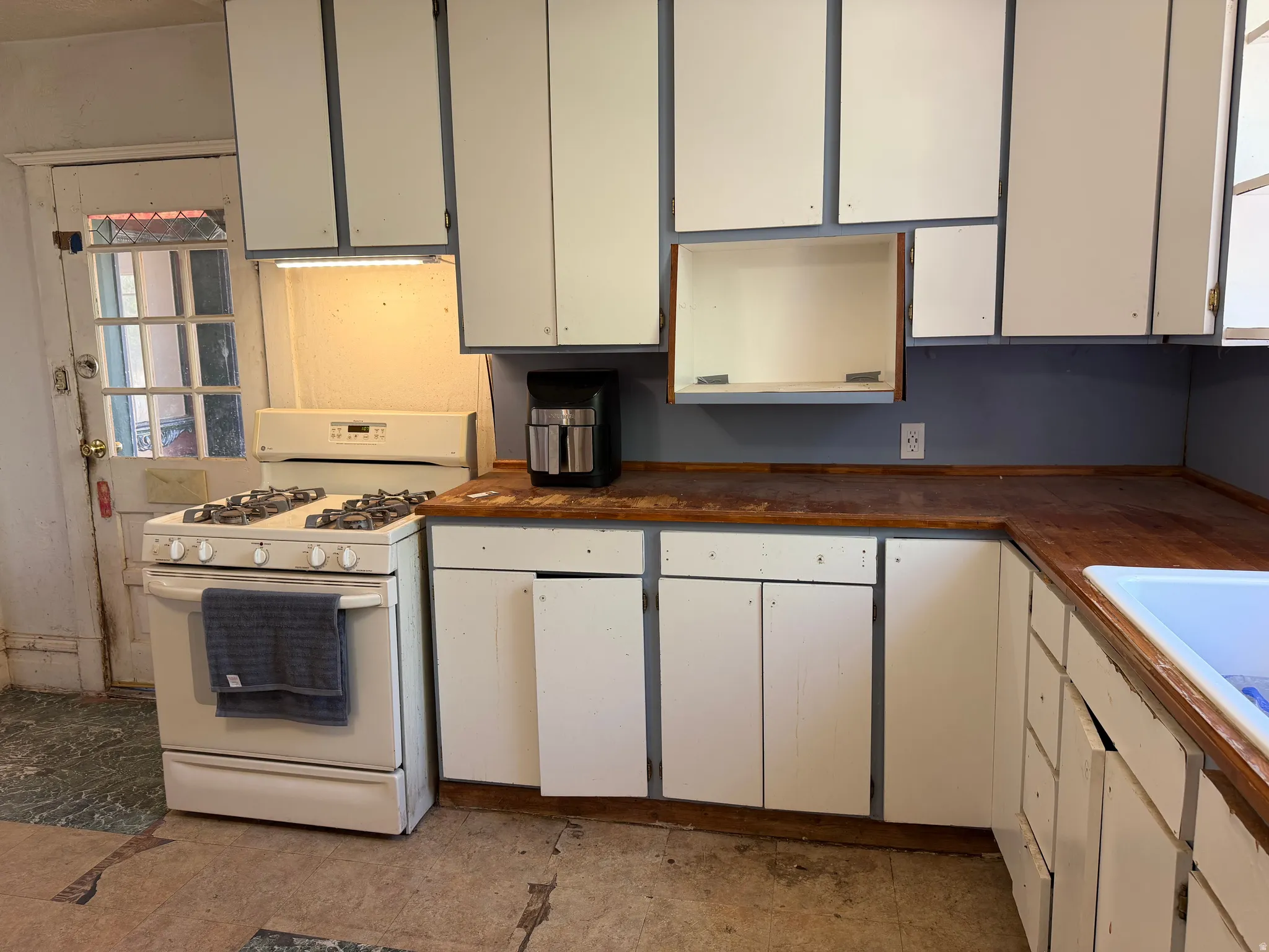 Kitchen featuring a white gas range, wood-finish countertops, and white upper and lower cabinetry