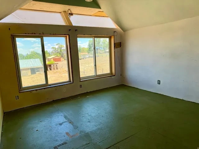Room featuring multiple windows, a sloped ceiling with exposed structural elements, and an unfinished floor