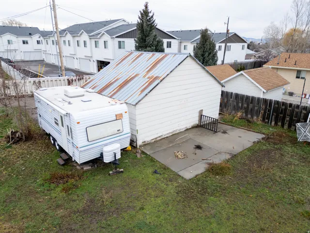 Detached garage structure with a weathered metal roof and white siding