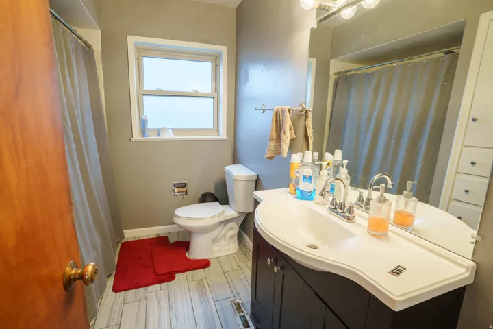Bathroom featuring a dark wood-finish vanity with an integrated white sink, a chrome faucet, and a large wall-mounted mirror with overhead lighting