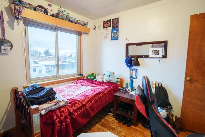 Bedroom featuring a large window with a wood-finish sill, light wood-finish flooring, a wood door, and white walls