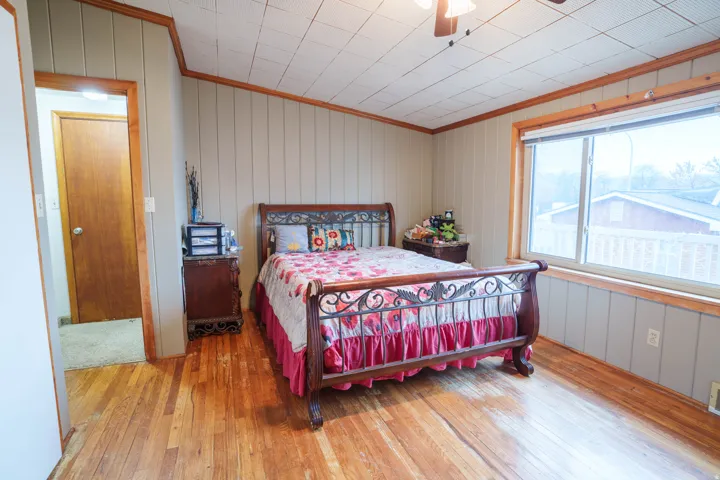 Bedroom featuring wood-finish flooring, vertical paneling, and a large window