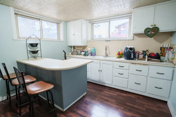 Kitchen area featuring a curved breakfast bar, white cabinetry, a stainless steel sink with a gooseneck faucet, and wood-finish flooring
