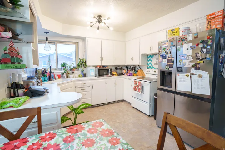 Bright kitchen featuring white cabinetry, a stainless steel French door refrigerator, a white electric range, a corner sink with window, and a modern ceiling light fixture