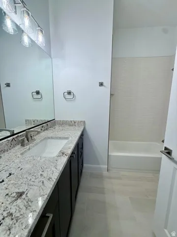 Bathroom featuring a vanity with a white granite countertop, undermount sink, dark wood-finish cabinetry, and a full-width mirror