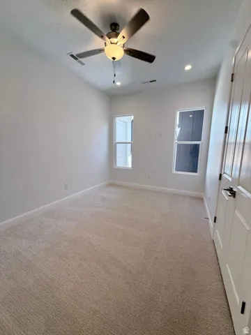 Neutral tone carpeted room featuring a ceiling fan with integrated lighting, two recessed ceiling lights, and two windows