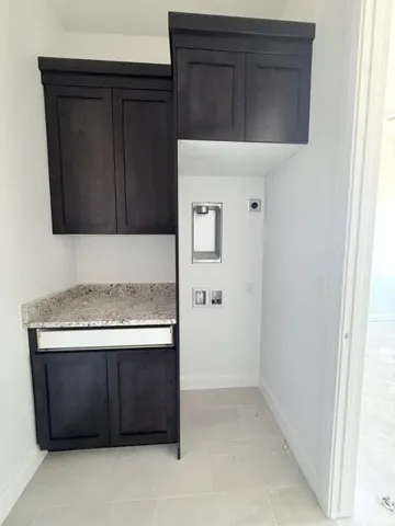Laundry area featuring dark wood-finish cabinetry, a stone countertop, and light-toned tile flooring