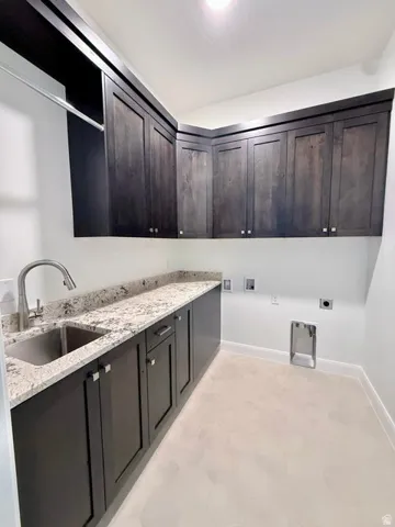 Laundry room featuring dark wood-finish cabinetry, light-toned countertops, a stainless steel sink with a brushed nickel faucet, and light-colored flooring