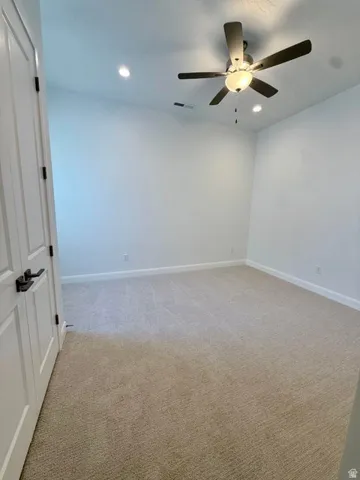 Carpeted interior room featuring a ceiling fan with integrated lighting, recessed ceiling lights, white walls, and white baseboards