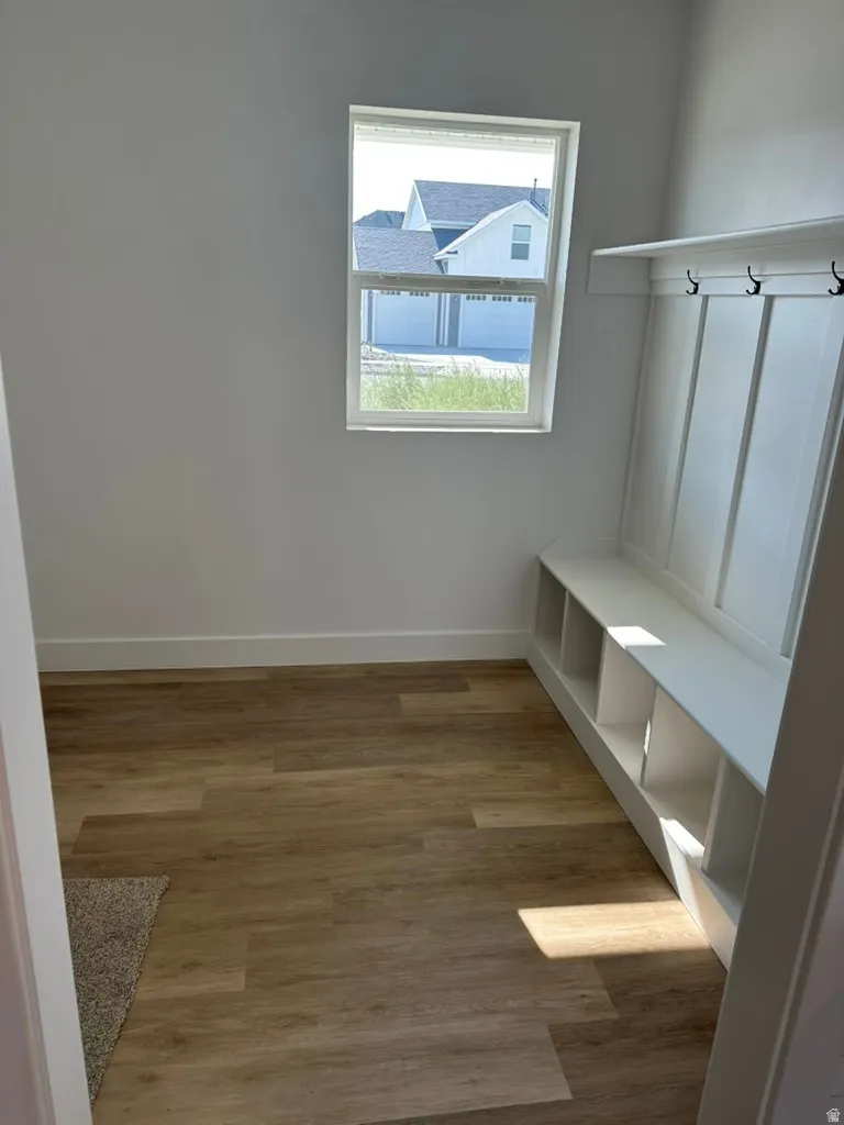 Built-in storage bench with cubbies and wall hooks, wood-finish flooring, white baseboards, and a framed window