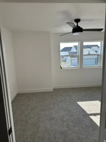 Bright room featuring two windows, a ceiling fan, plush gray carpeting, and a built-in white cabinet with panel detailing