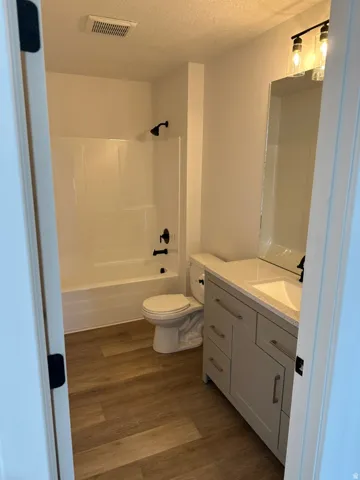 Contemporary bathroom featuring a white tub/shower combination with matte black fixtures, a single-sink vanity with a light-colored countertop, and wood-finish flooring