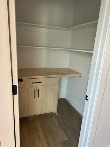 Built-in cabinetry with modern black hardware, light wood-finish countertop, white shelving, and wood-finish flooring