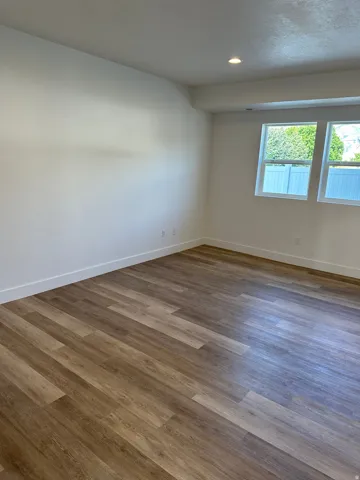 Spacious room featuring wood-finish flooring, white baseboards, recessed ceiling lighting, and two casement windows with white frames