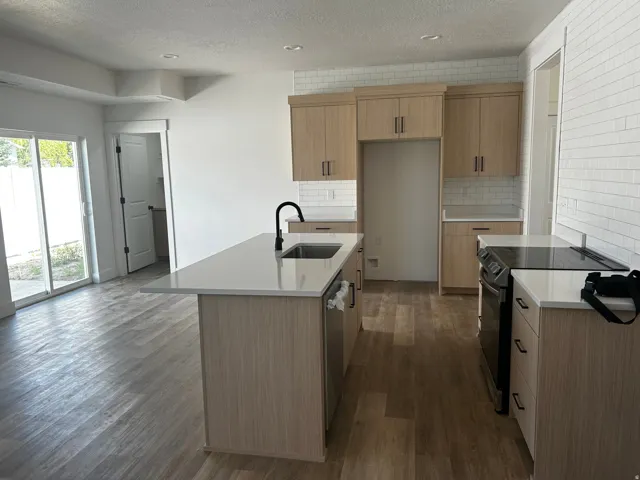 Kitchen featuring an island with an undermount sink, light wood-finish cabinetry, subway tile backsplash, and a flat-top electric range