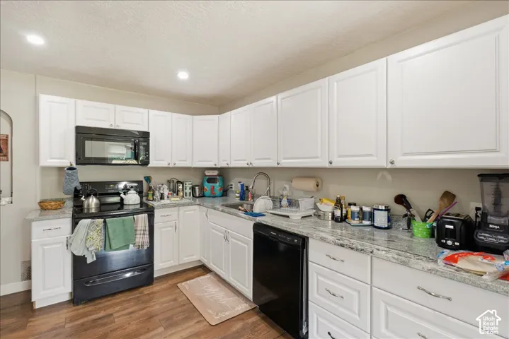Kitchen featuring white cabinetry, light-toned countertops, a black range with an above-range microwave, a built-in dishwasher, and wood-finish flooring