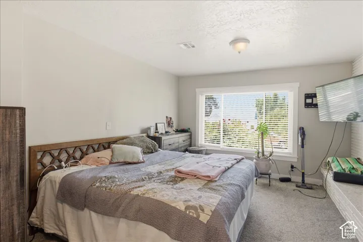 Spacious room featuring light gray walls, textured ceiling, a large window with white blinds and trim, and gray carpeting