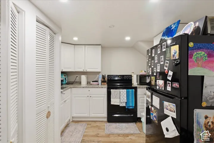 Compact kitchen featuring white cabinetry, light-colored countertops, black appliances, recessed lighting, and wood-finish flooring