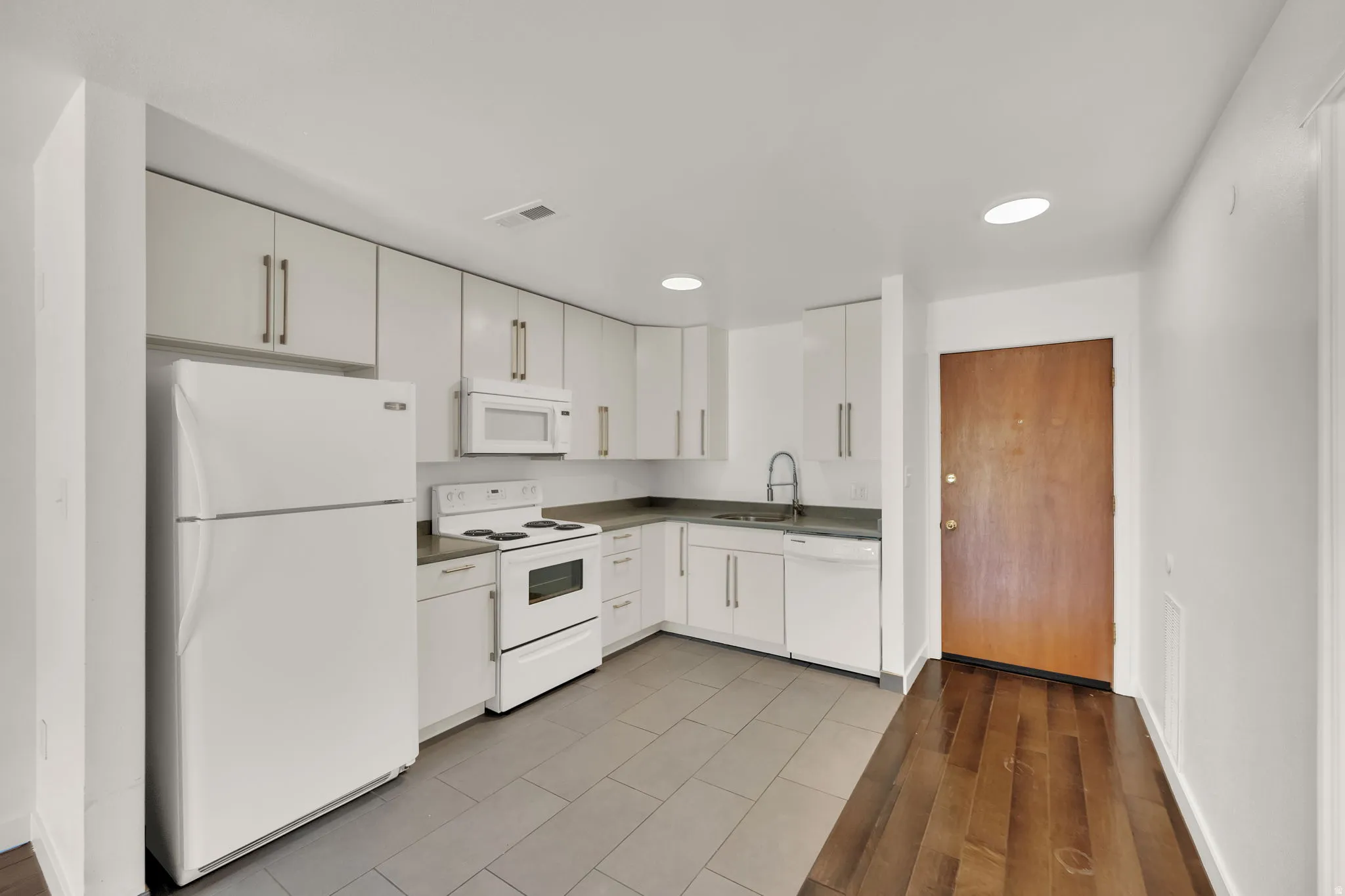 Kitchen featuring white cabinetry, grey countertops, and white appliances including a refrigerator, range, microwave, and dishwasher