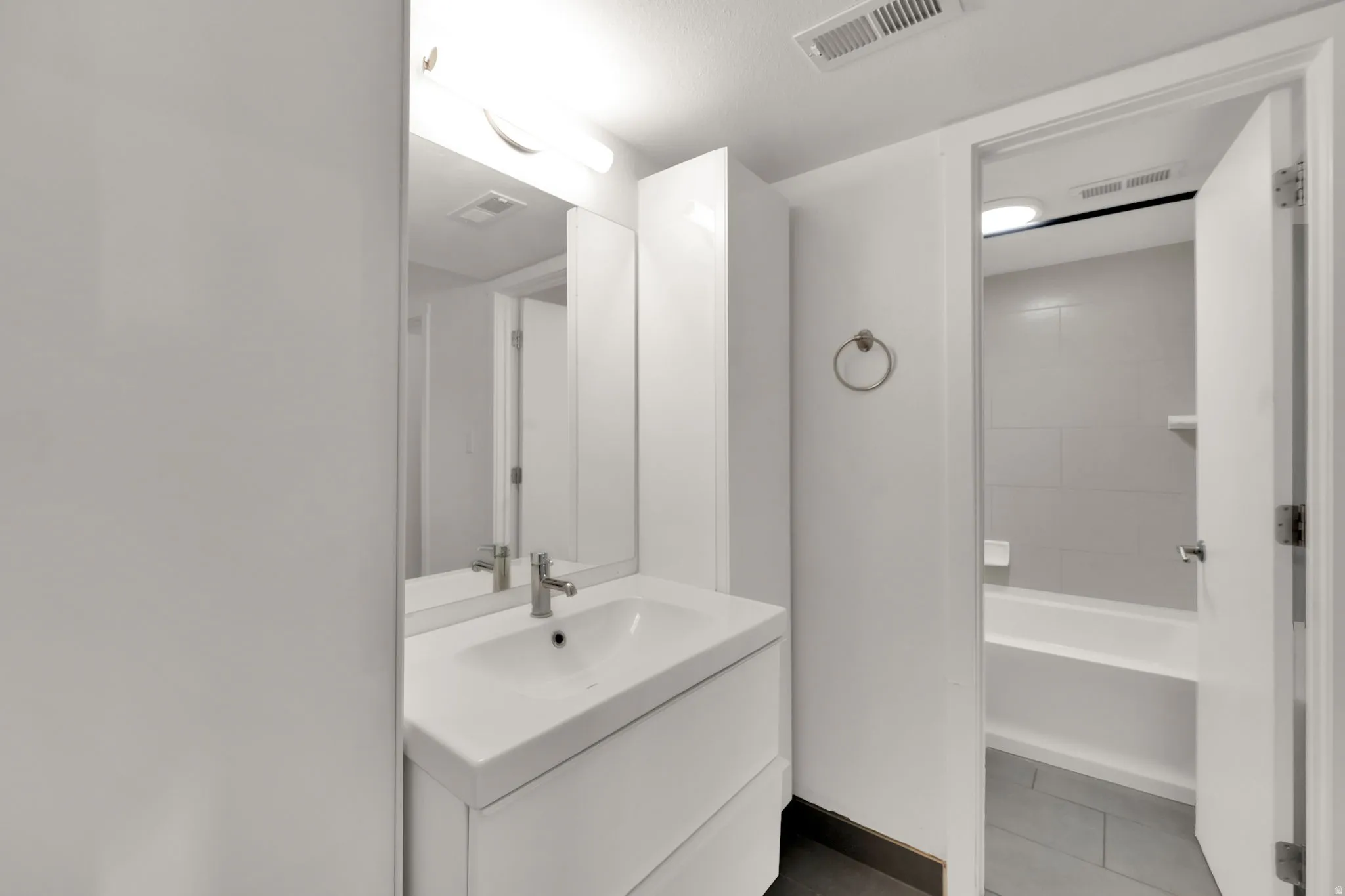 Bathroom featuring a white vanity with integrated sink, chrome faucet, and mirrored medicine cabinet