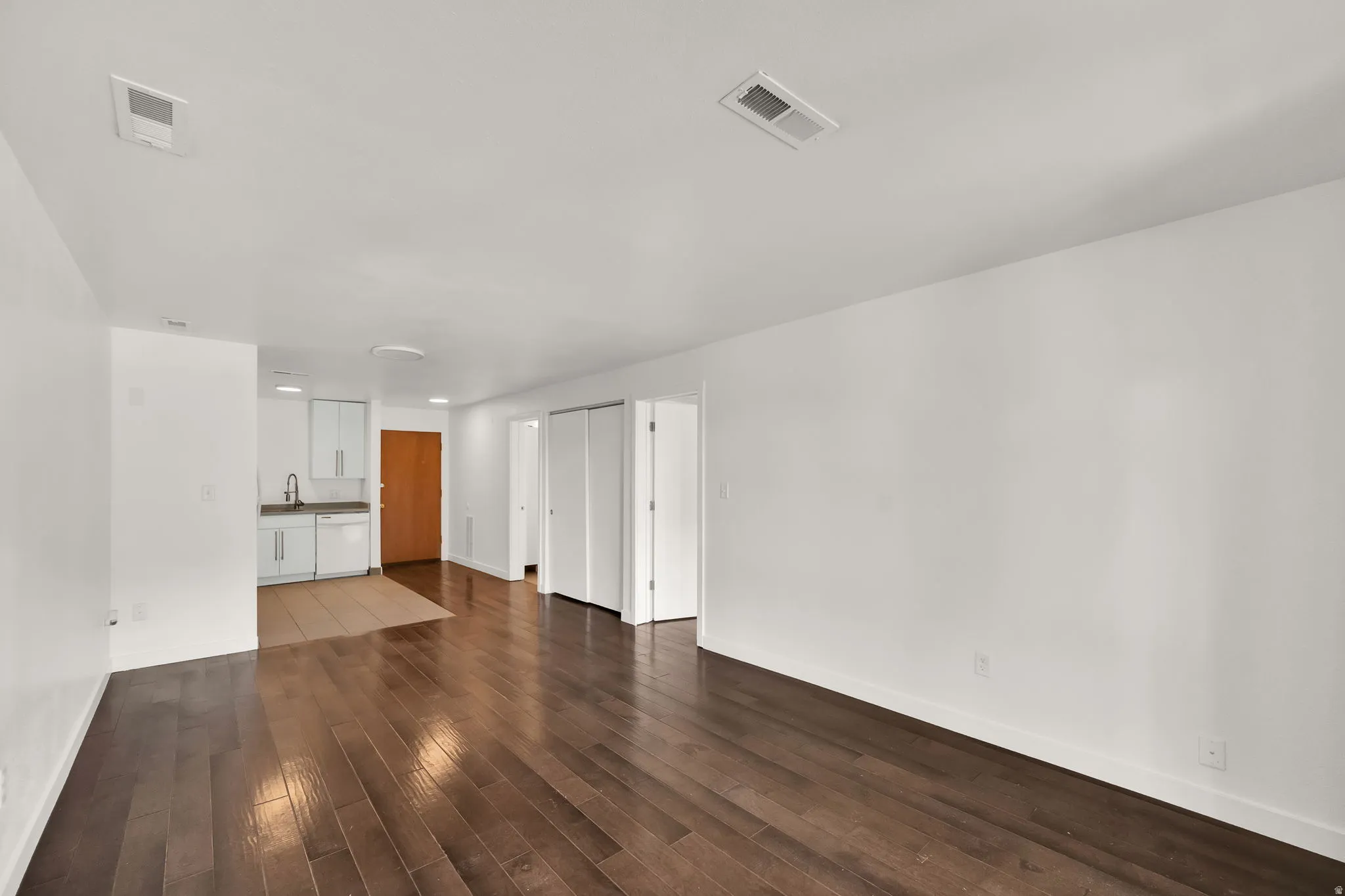 Spacious room featuring dark wood-finish flooring, white walls, and a recessed ceiling light