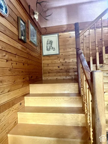 Staircase featuring wood-paneled walls, wooden treads, and a wooden banister with turned balusters