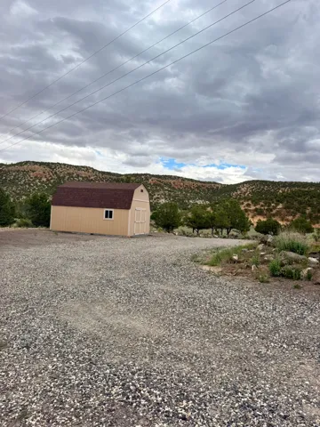 Freestanding storage shed with gambrel roof and a single window, set on a gravel lot