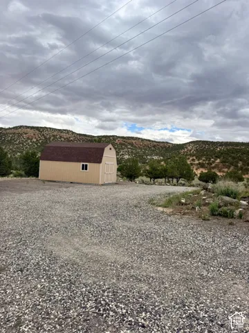 Freestanding storage shed with gambrel roof and a single window, set on a gravel lot