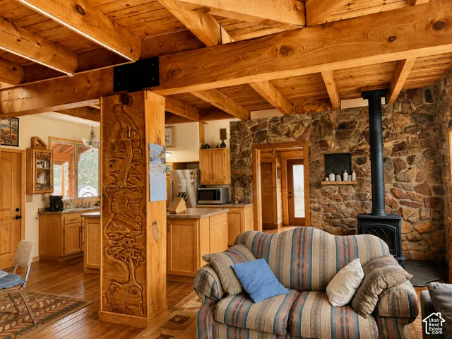 Exposed wood beam ceiling, wood-finish flooring, stone accent wall, black wood-burning stove, and carved wood pillar
