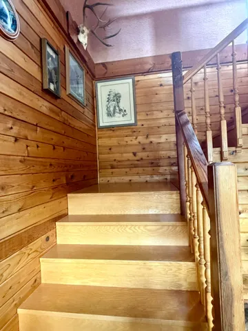 Staircase featuring wood-paneled walls, wooden treads, and a wooden banister with turned balusters