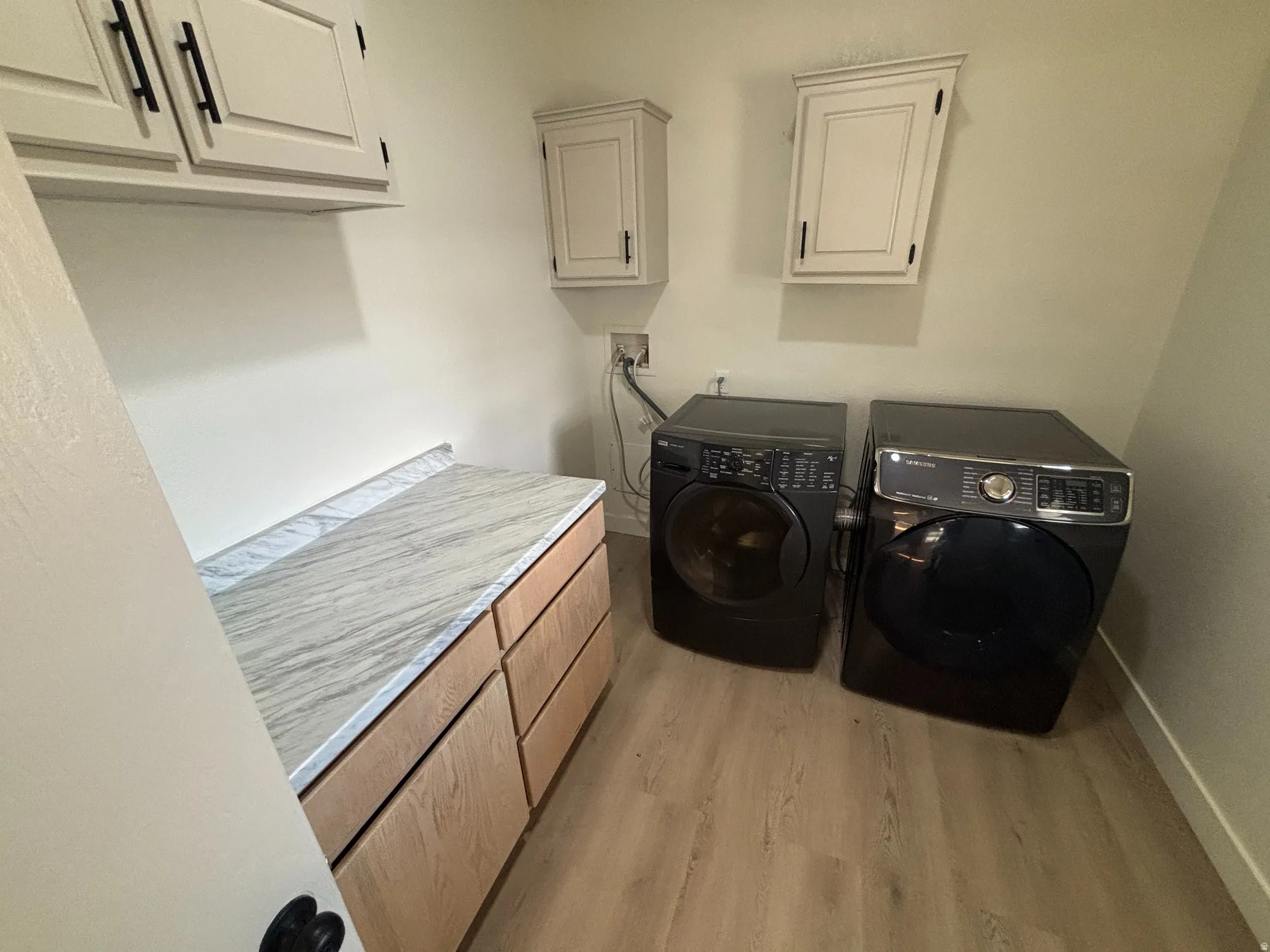 Laundry area featuring light wood-finish flooring, light gray walls, and a built-in counter with a marble-look surface