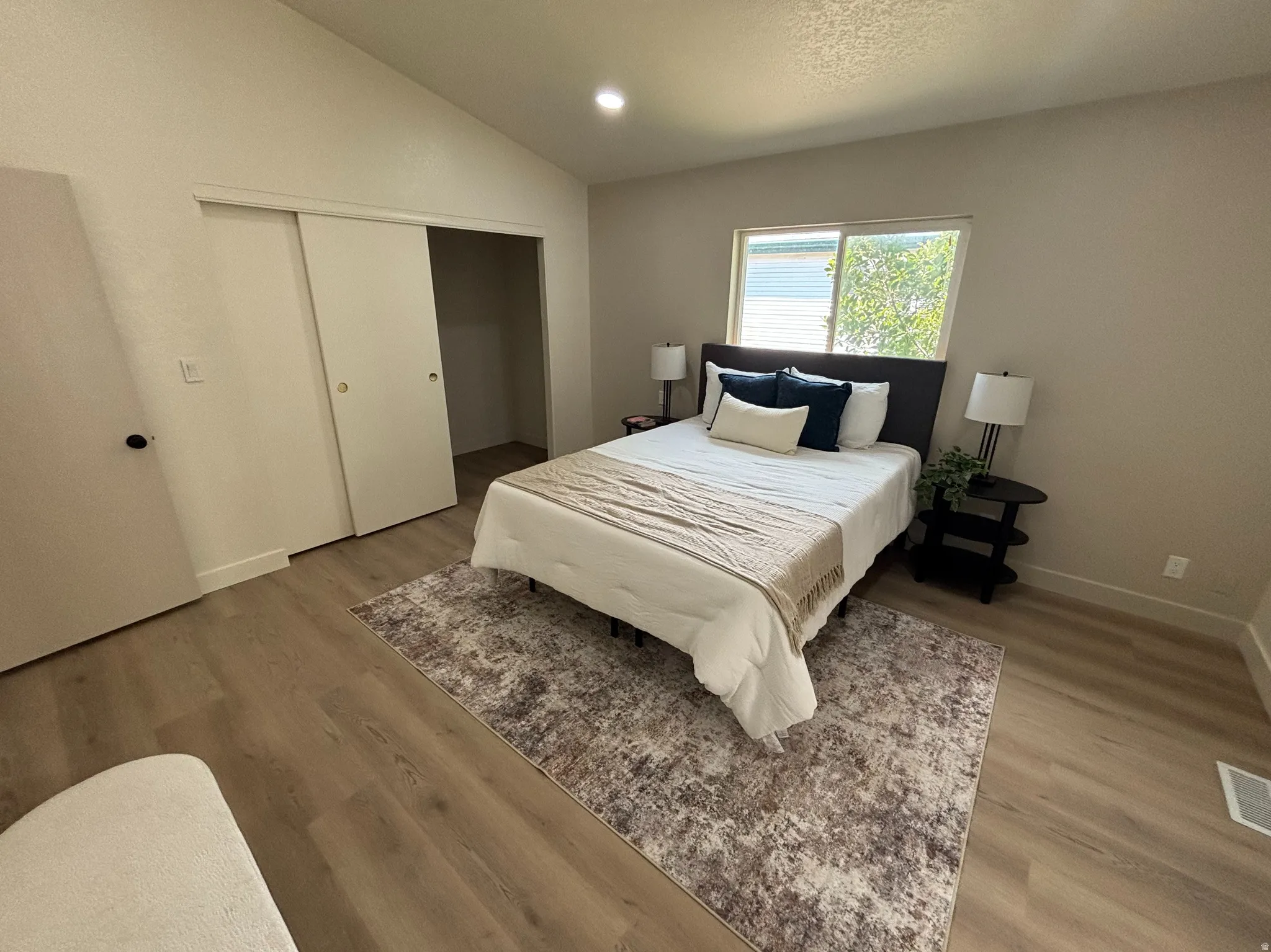 Room featuring vaulted ceilings, wood-finish flooring, and light-toned walls