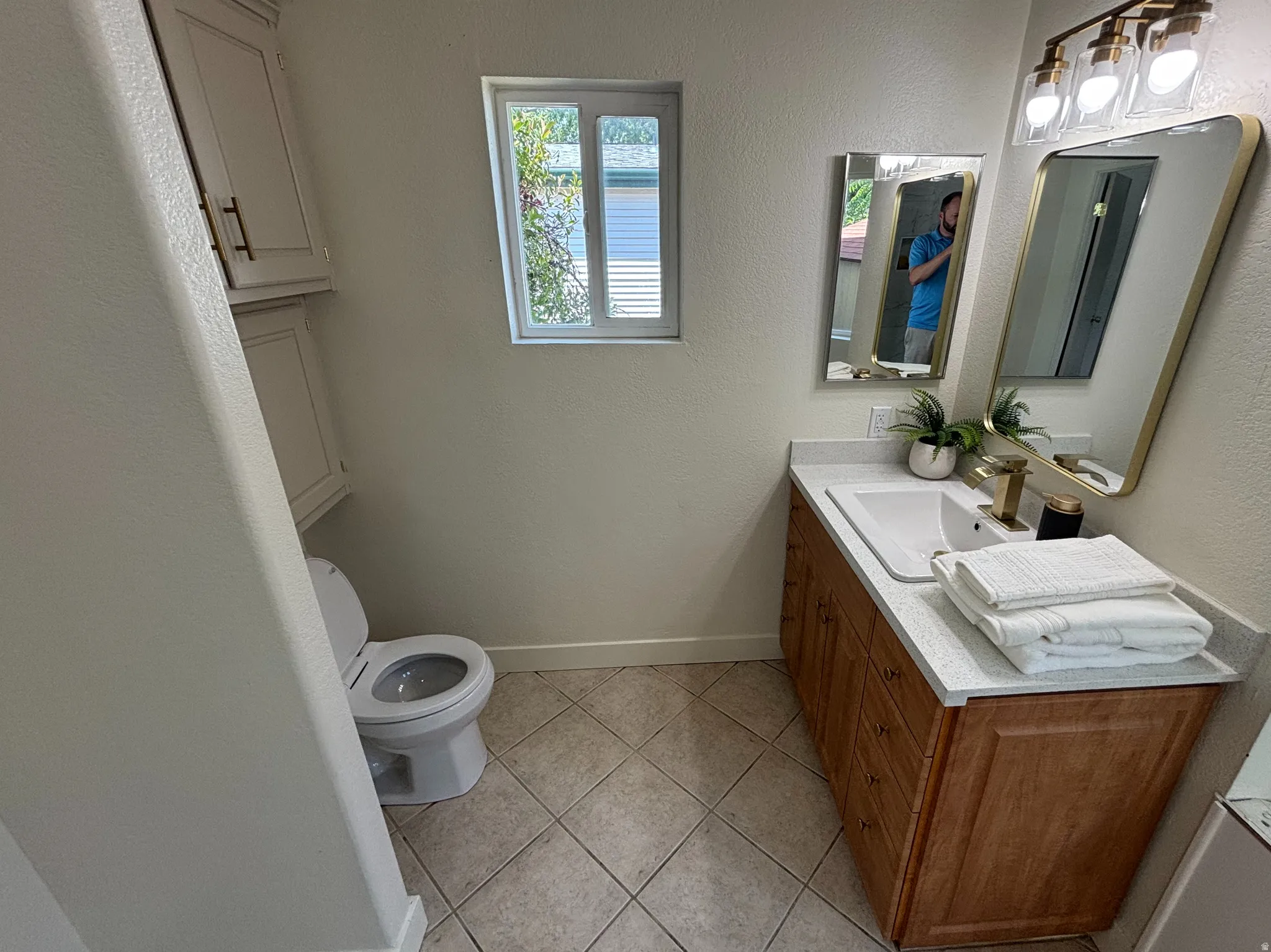 Bathroom featuring a single vanity with a light-colored countertop, wood-finish cabinetry, and a rectangular sink with a gold-tone faucet