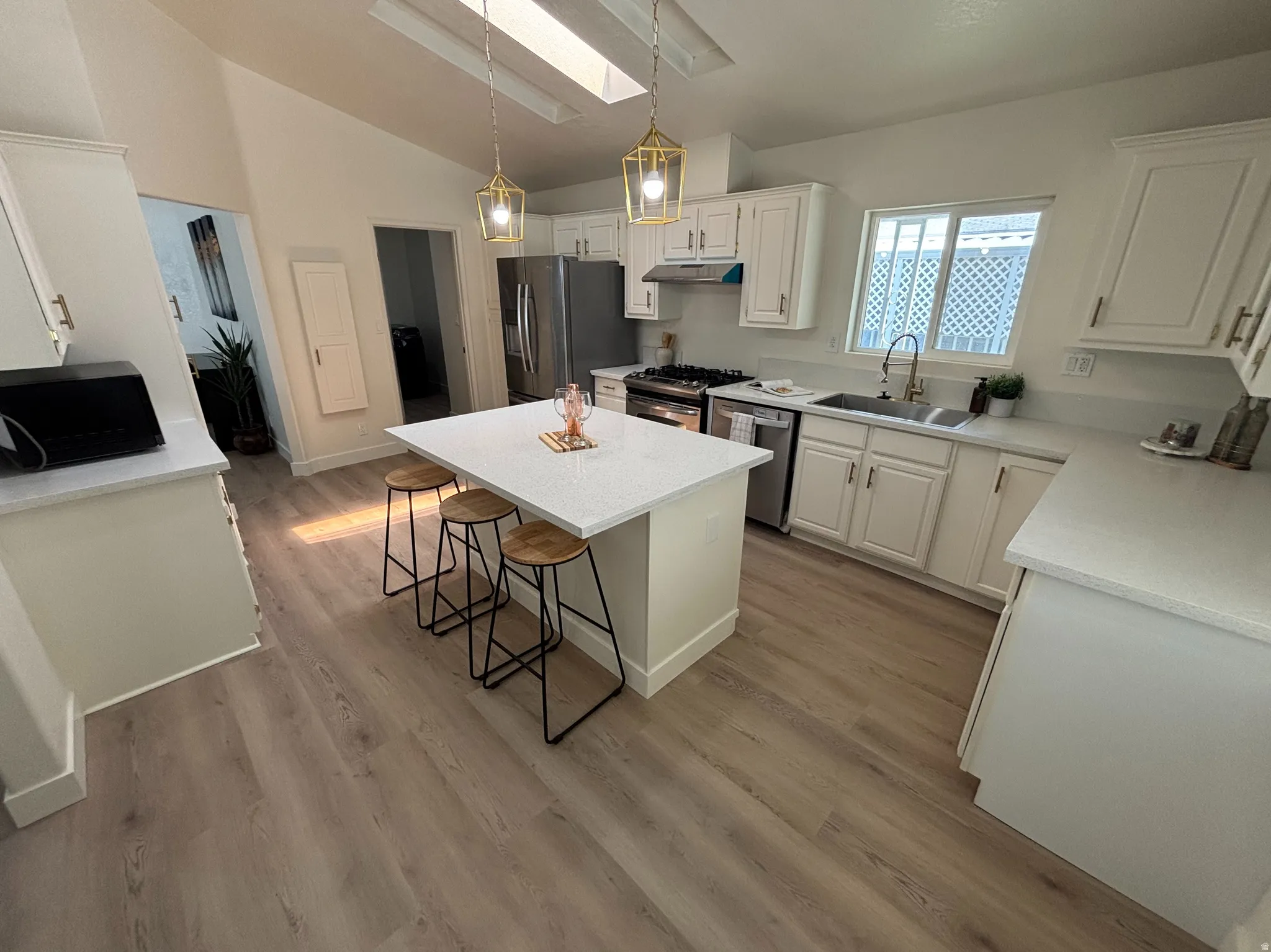 Open-concept kitchen featuring an island with counter seating, wood-finish flooring, white cabinetry with silver-tone hardware, and stainless steel appliances