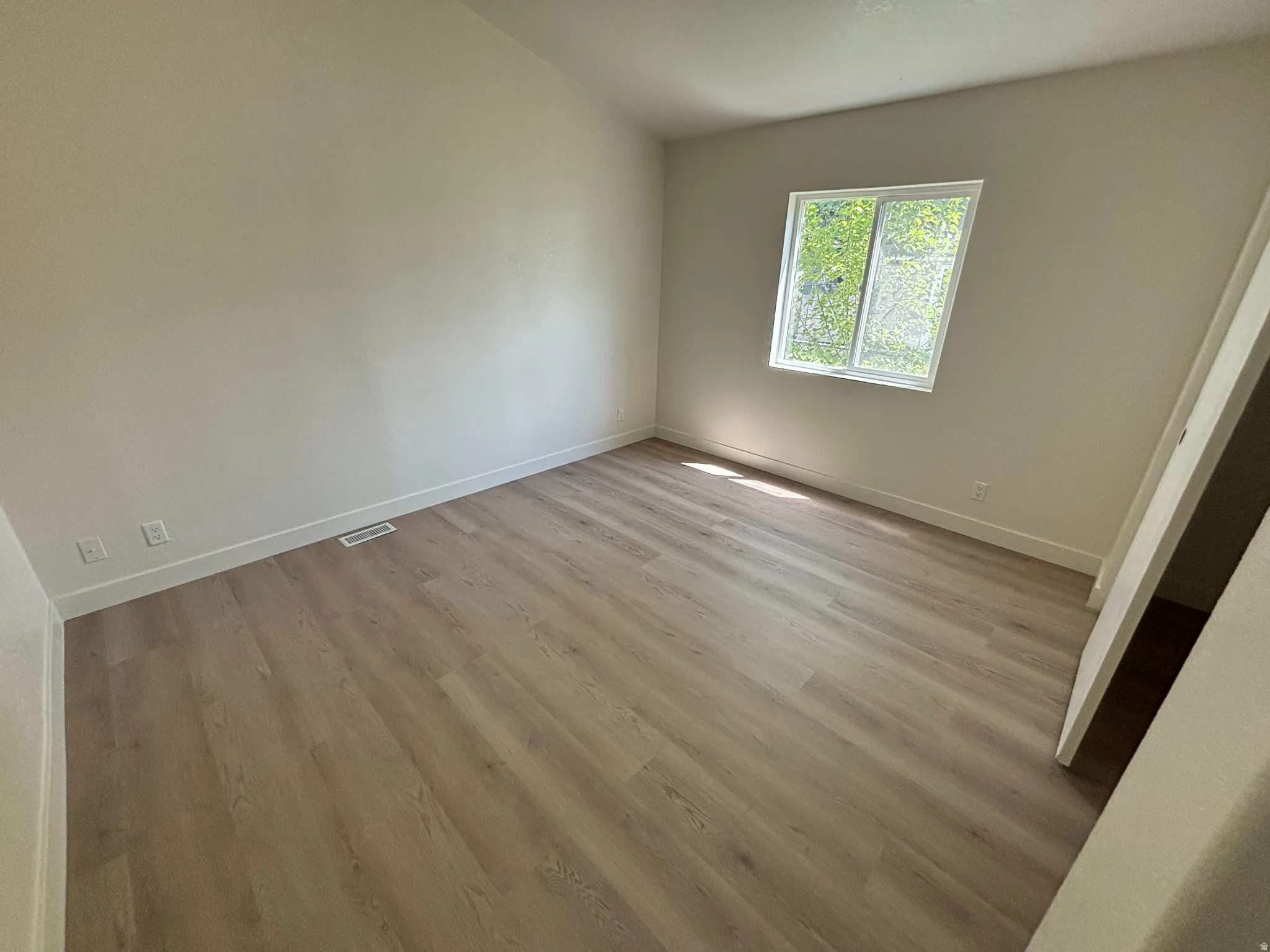 Room featuring light-toned walls, wood-finish flooring, and a single window