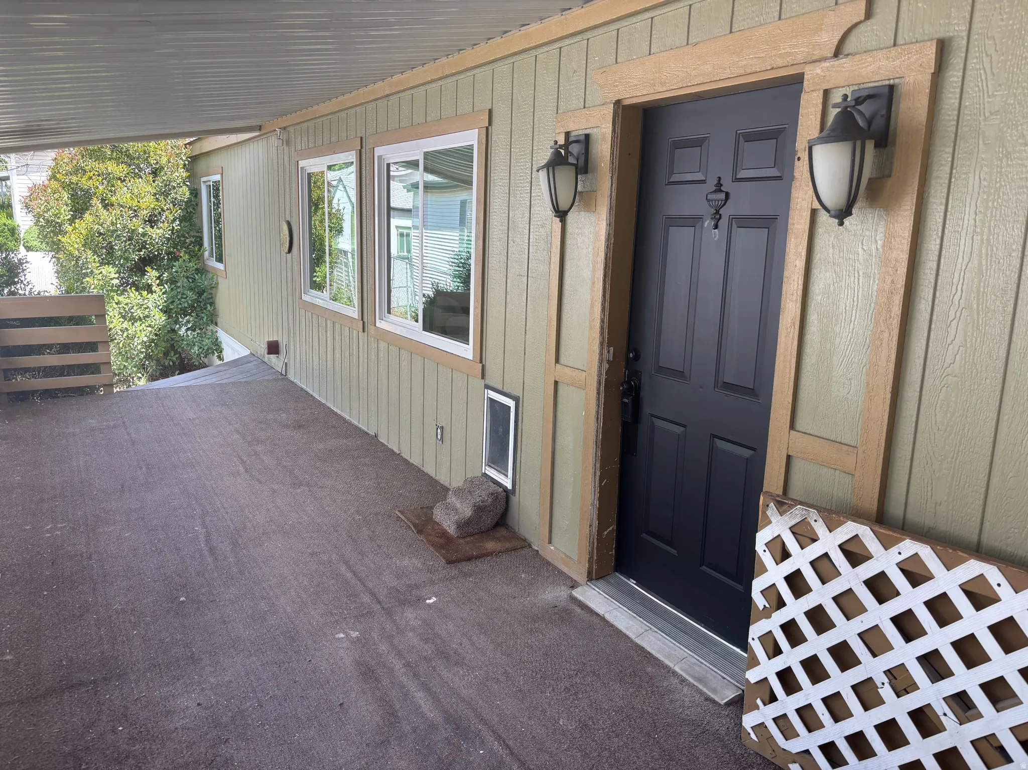 Covered entryway featuring a black paneled door with decorative trim and dual exterior sconces