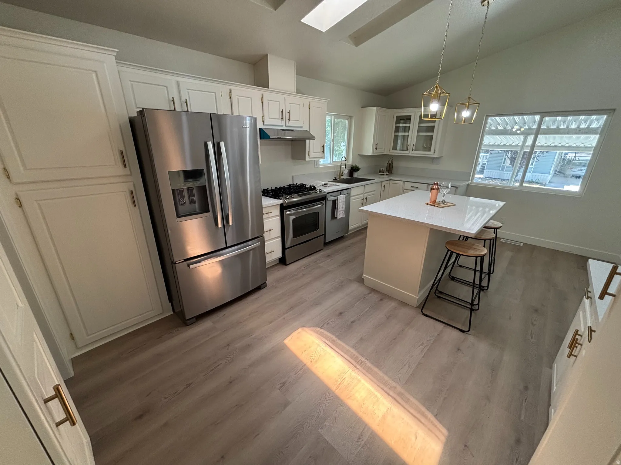 Kitchen featuring white cabinetry, stainless steel appliances, a center island with a white countertop, and wood-finish flooring