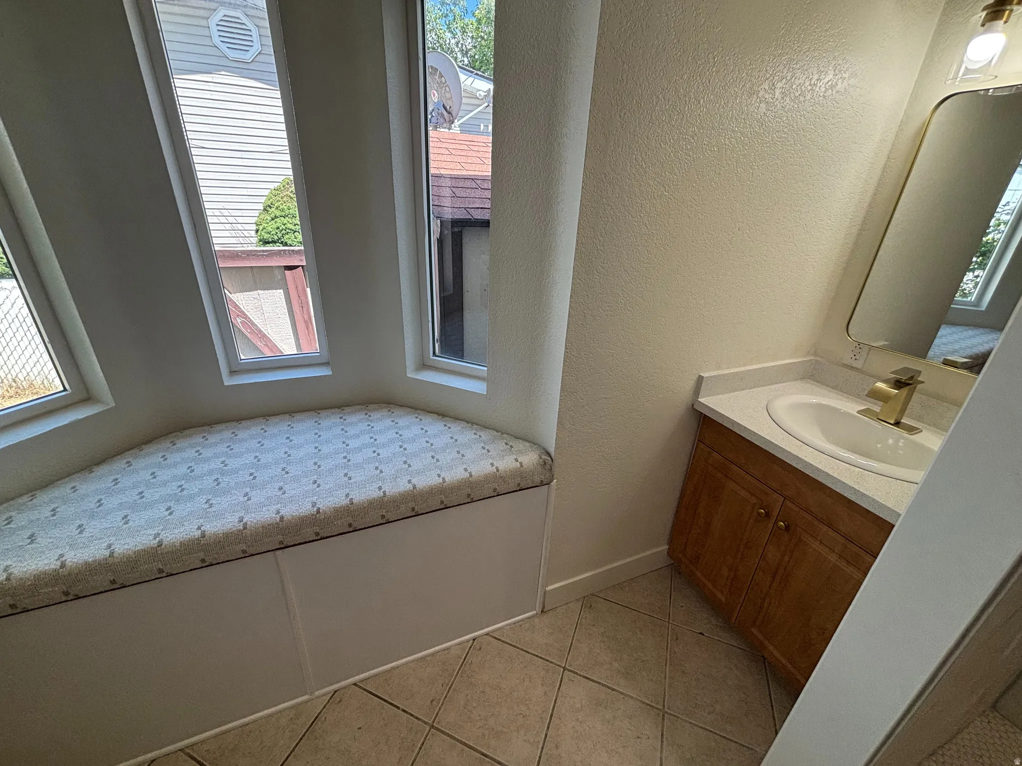 Built-in window bench with three vertical windows, accompanied by a vanity featuring a gold-finish faucet and an integrated sink with a light-toned countertop