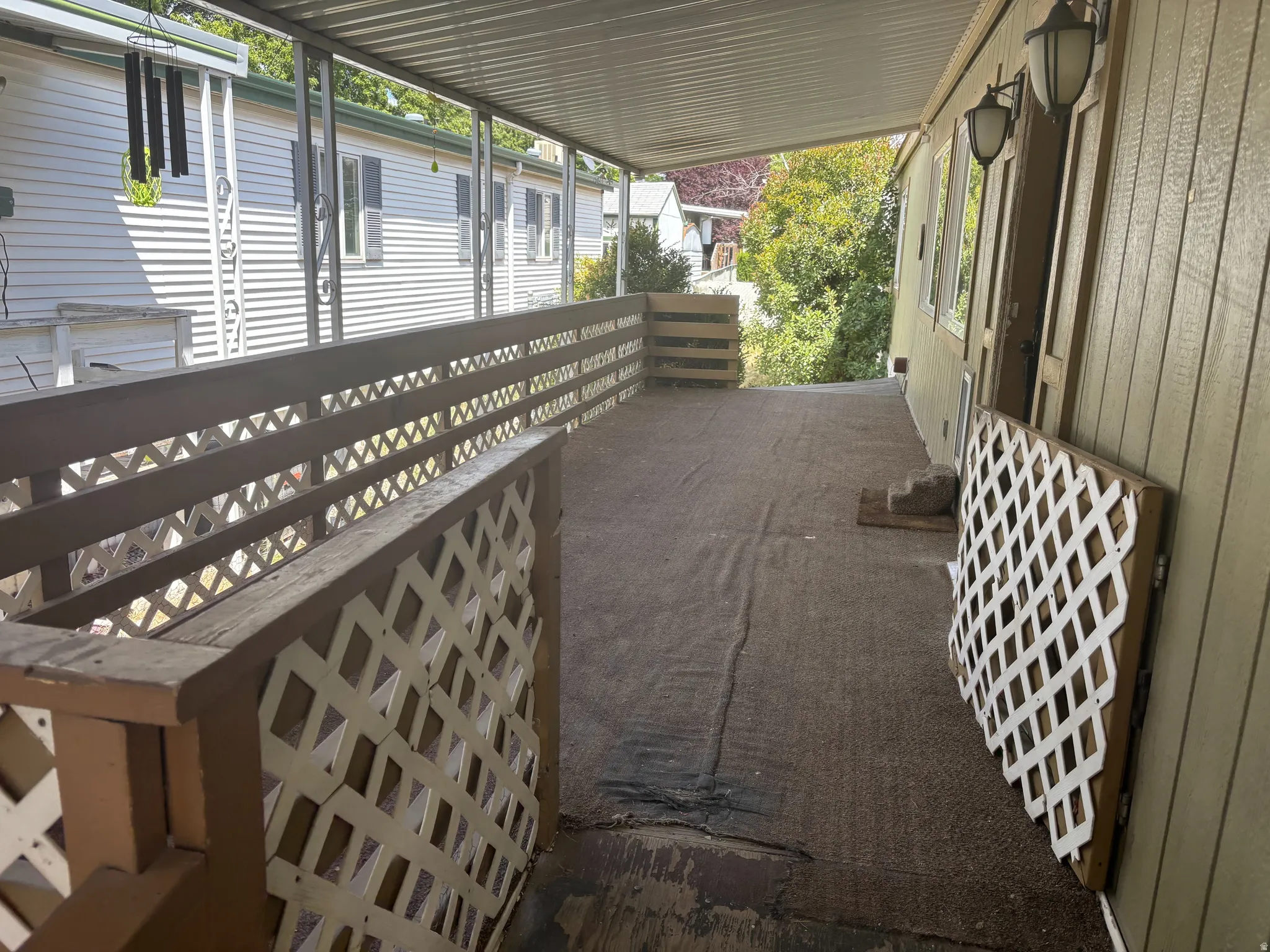 Covered outdoor patio area featuring a textured floor surface, lattice railing, and exterior wall lanterns