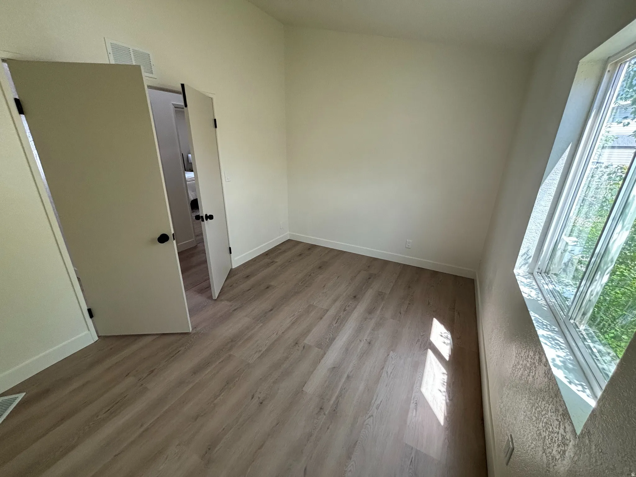 Room featuring wood-finish flooring, white walls, and a large window