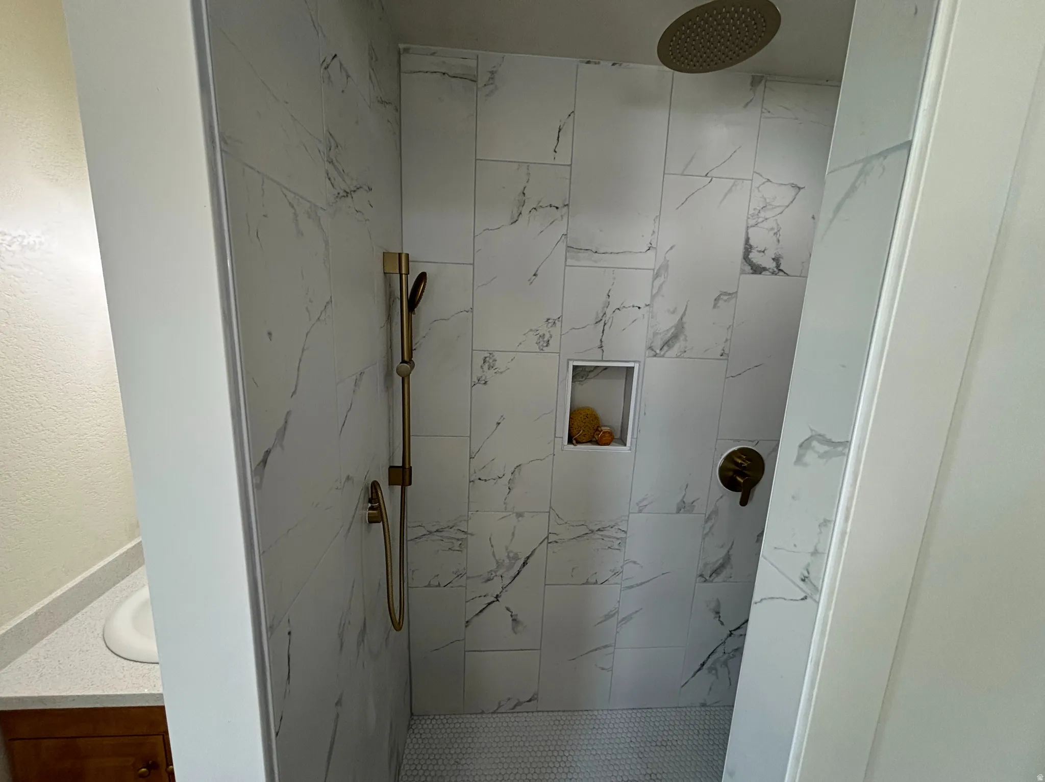 Walk-in shower featuring large format marble-look tile, a rain shower head, a handheld shower fixture, a recessed niche, and a hexagonal mosaic tile floor