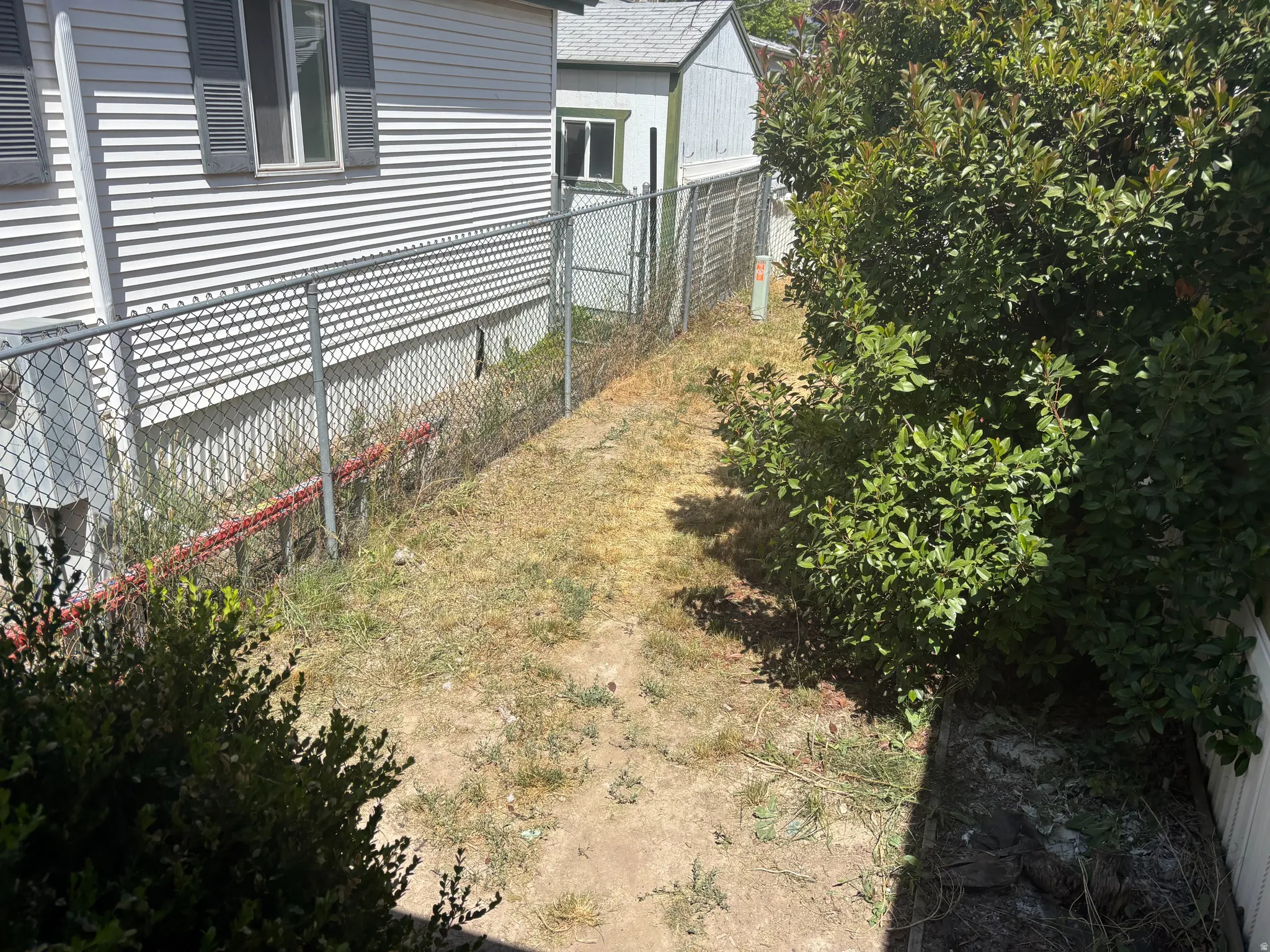Side yard featuring a chain-link fence separating the property from an adjacent structure