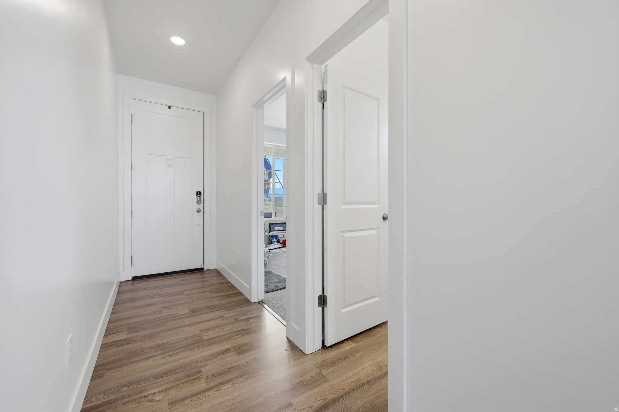 Entryway featuring wood-finish flooring, recessed lighting, white trim, a white paneled door with modern hardware, and a white interior door