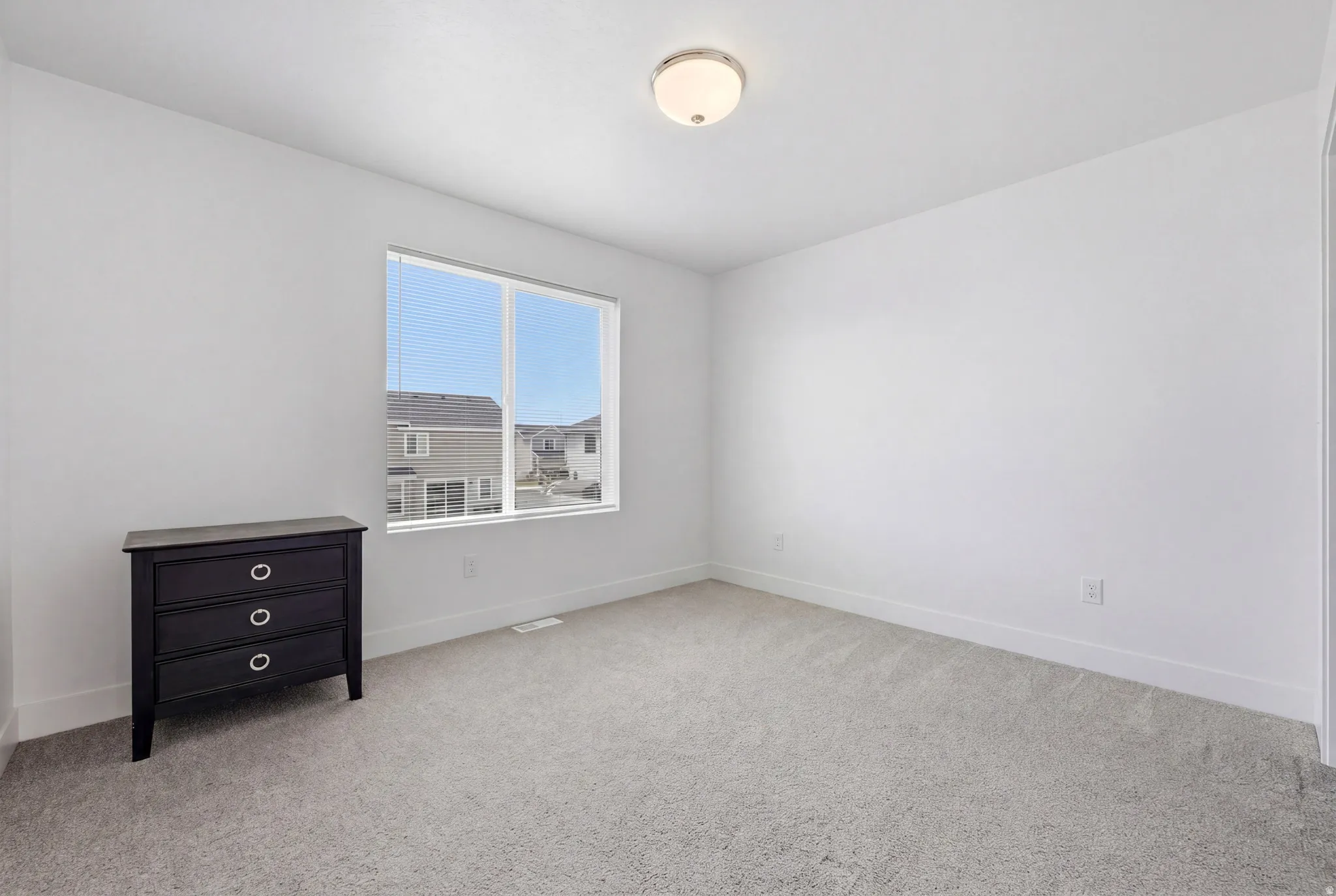 Windowed interior space featuring light-colored walls, grey carpeting, and white baseboards
