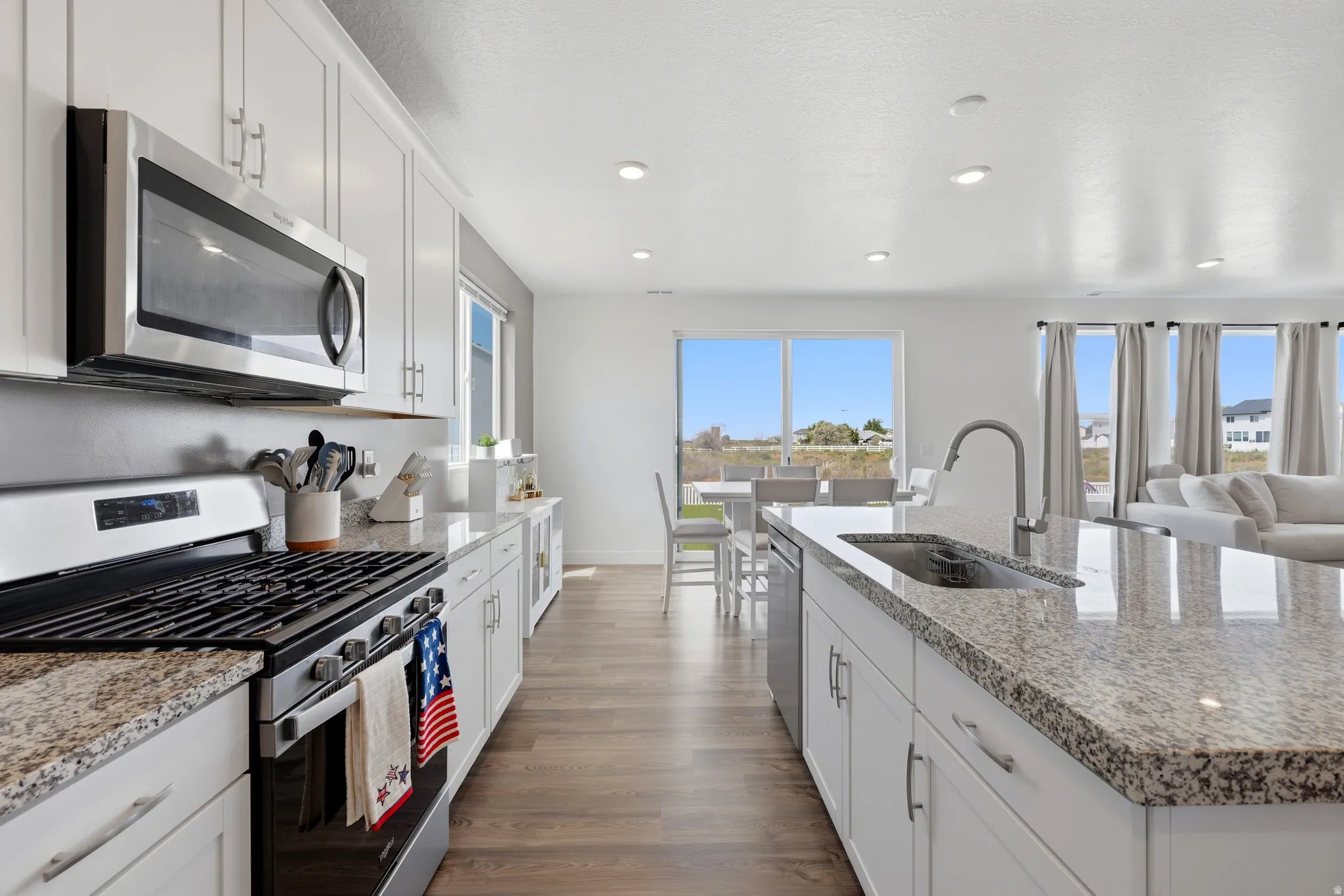 Modern kitchen featuring stainless steel appliances, granite countertops, white cabinetry, and wood-finish flooring