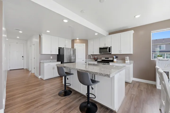 Modern kitchen featuring white cabinetry, light-colored granite-style countertops, stainless steel appliances, and wood-finish flooring