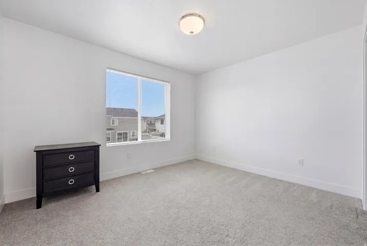 Windowed interior space featuring light-colored walls, grey carpeting, and white baseboards
