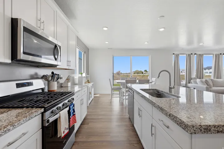 Modern kitchen featuring stainless steel appliances, granite countertops, white cabinetry, and wood-finish flooring