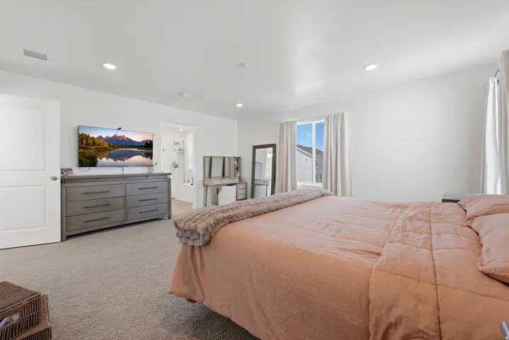 Spacious bedroom featuring light-colored carpet flooring, recessed lighting, and a white interior door